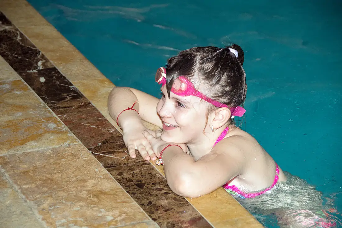 Fetiță cu ochelari de înot la marginea piscinei