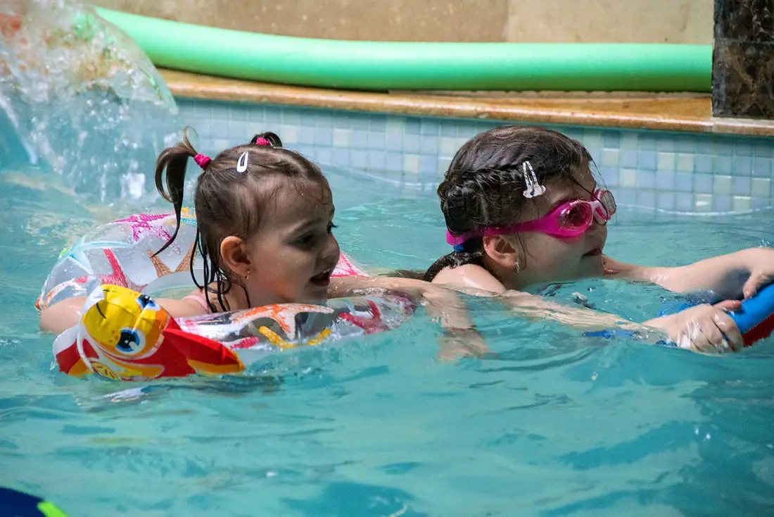 Două fetițe înotând în piscina încălzită